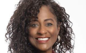 Woman with curly hair and gold earrings smiling in a close-up professional headshot against a white background