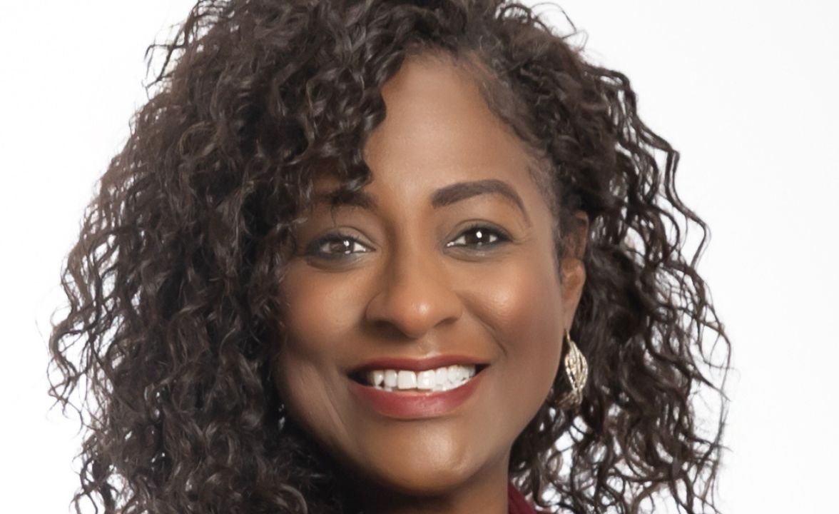 Woman with curly hair and gold earrings smiling in a close-up professional headshot against a white background