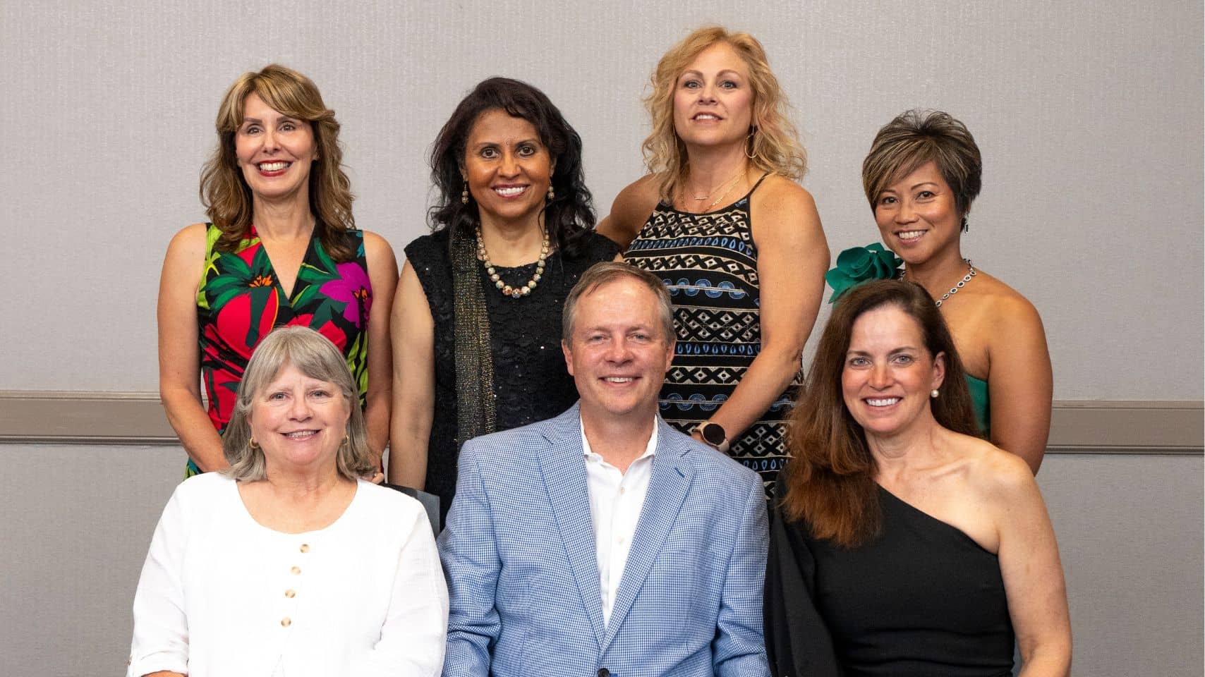 Seven alumni pose for a formal group photo at a PCOM event, three seated in front and four standing behind