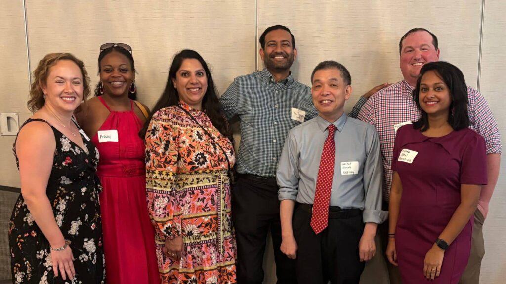 Seven alumni wearing name tags pose together smiling at a PCOM Georgia reunion event