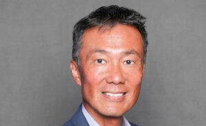 Man in a blue blazer smiling in a professional headshot against a gray background