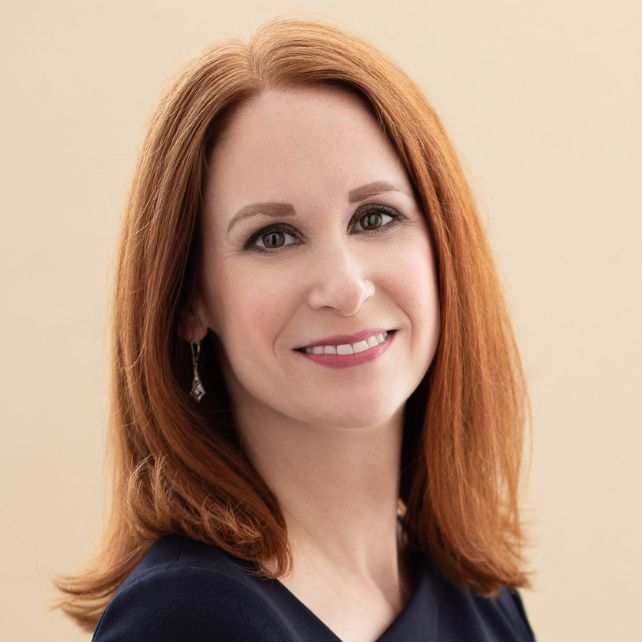 Carrie Collins smiling in a professional headshot against a warm beige background