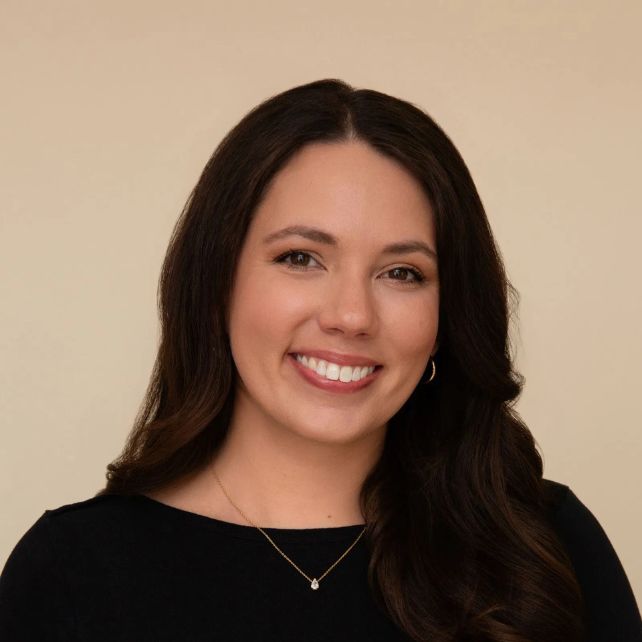 Meghan McCall smiling in a professional headshot wearing a black top and gold necklace against a beige background