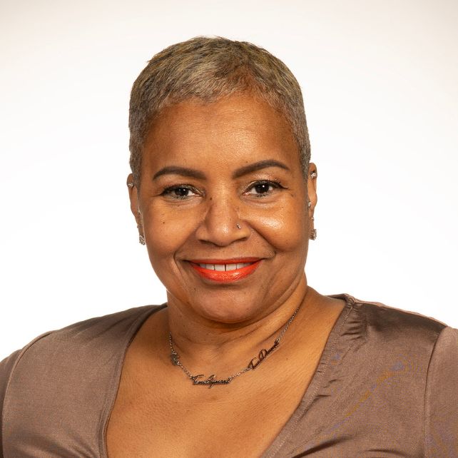 Traci Russell smiling in a professional headshot wearing a brown top and script necklace against a white background