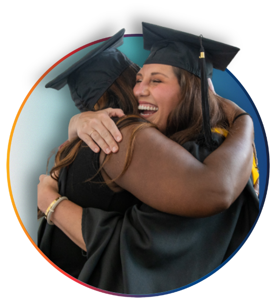 Two students in graduation gowns and hats smile and embrace in celebration