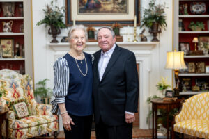 Sandra Strickland smiles in a blue blouse next to Clyde Strickland in a dark suit in front of a white fireplace.