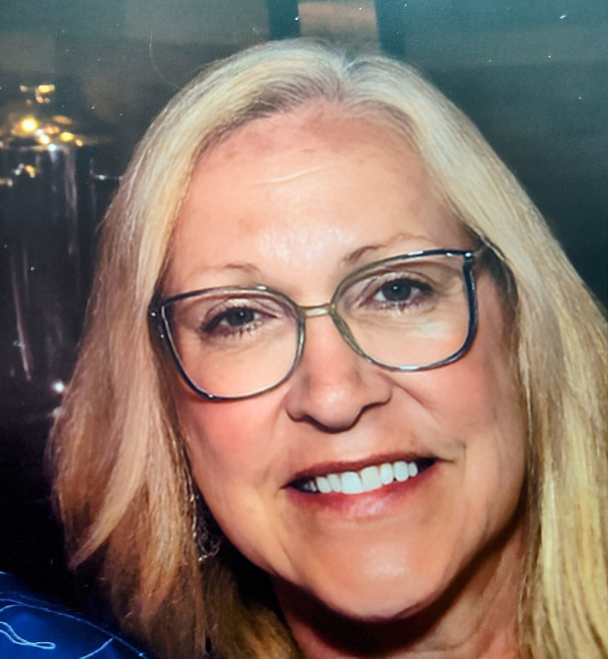 Deborah Manning smiling in glasses against a dark background.
