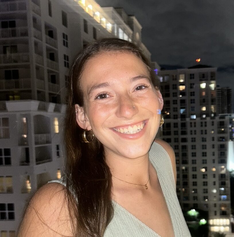 A female student in a green shirt smiles in front of a city skyline