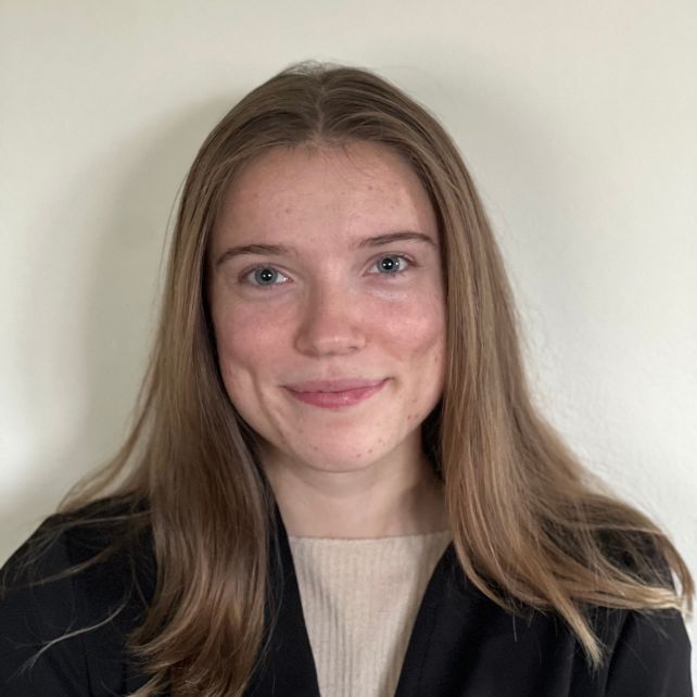 Alexis Martina smiling in a headshot wearing a black blazer and beige top against a neutral background