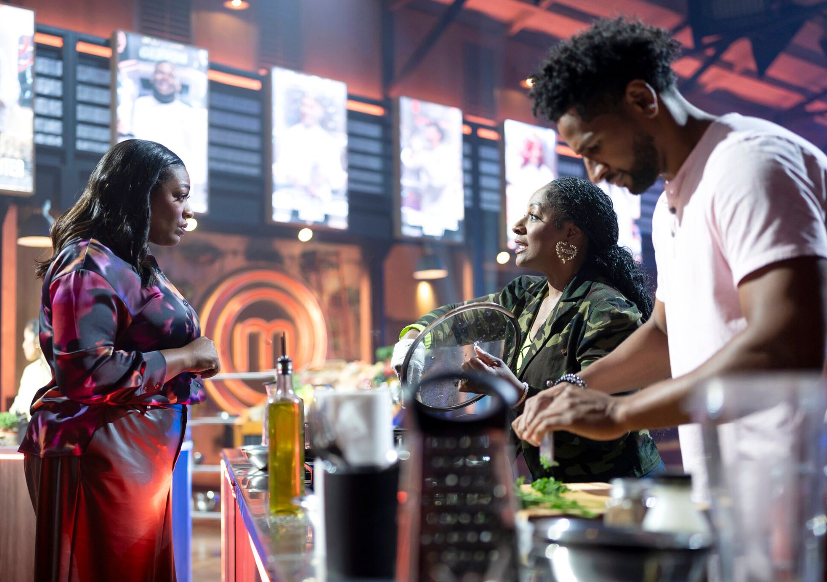 Three people conversing at a cooking station on a television competition set