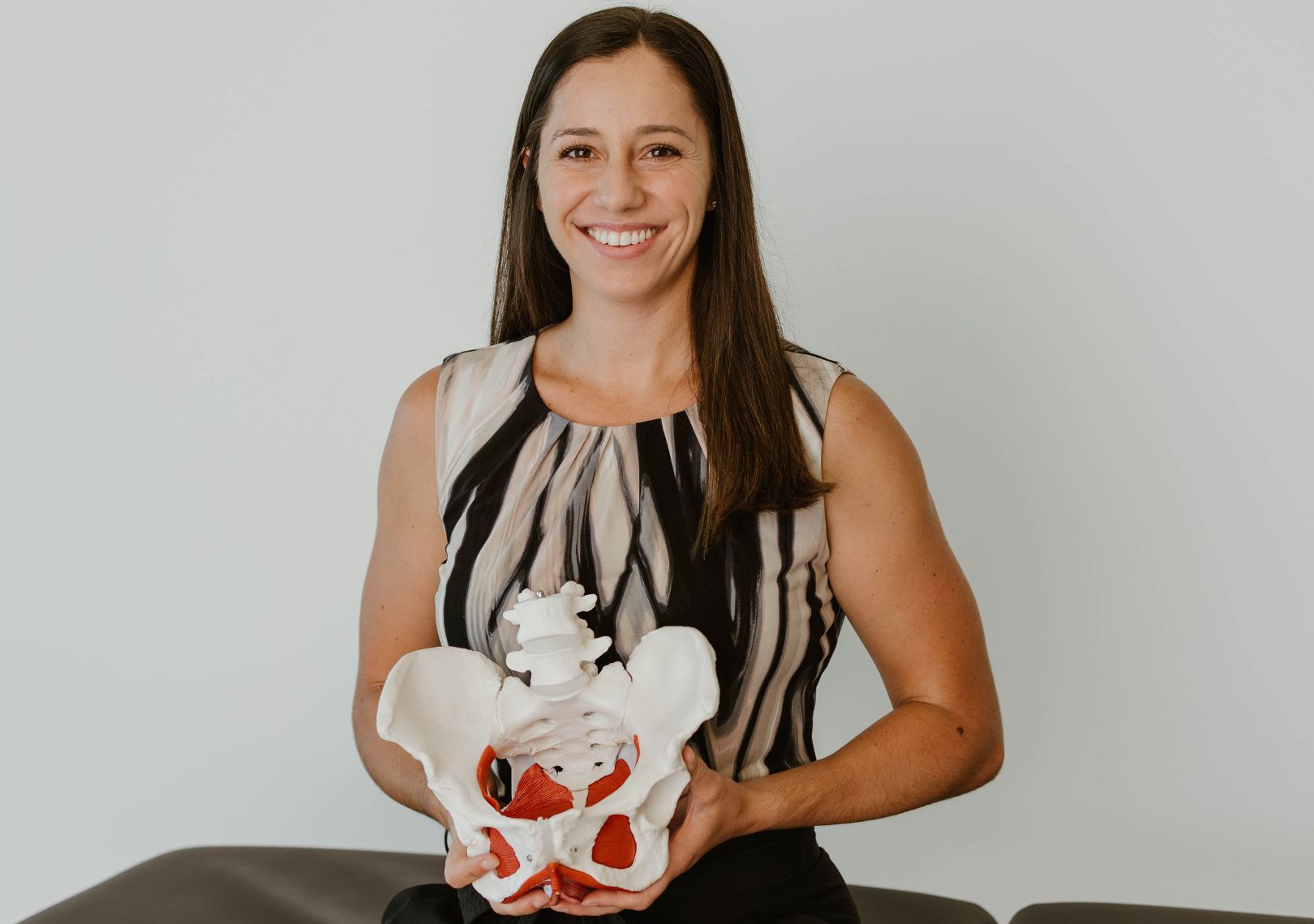 Woman smiling while holding an anatomical pelvic model in a clinical setting