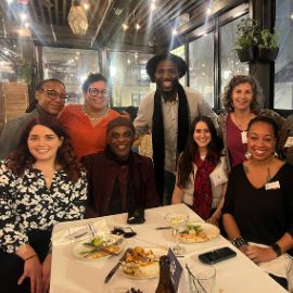 A group of eight alumni smile together at a dinner table during a PCOM alumni gathering at a restaurant