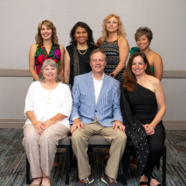 Seven alumni pose together for a group photo at a formal PCOM event with four standing and three seated