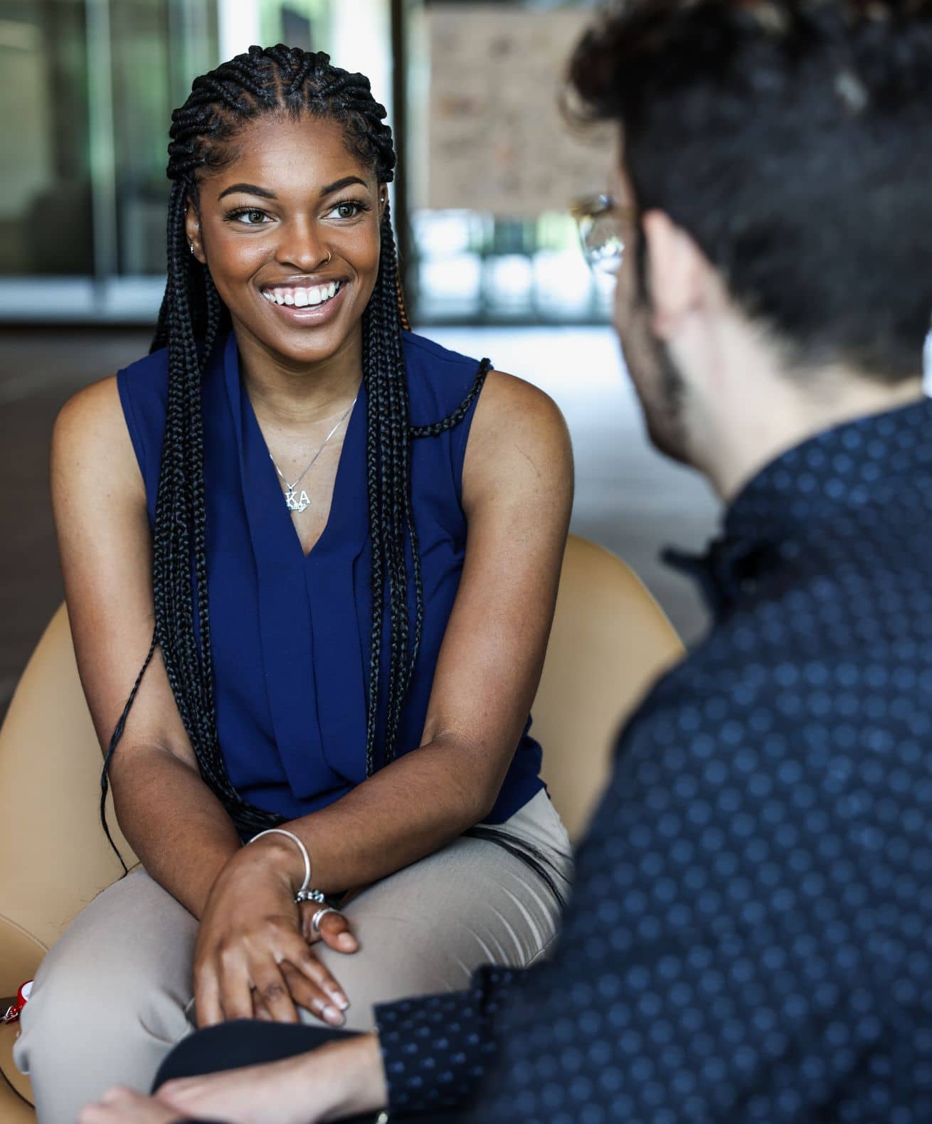 Young woman with braids in a navy blouse smiling during a one-on-one conversation in a modern office setting