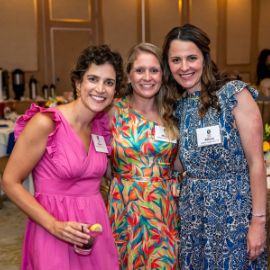 Three women wearing name tags pose together and smile at a PCOM alumni reunion event
