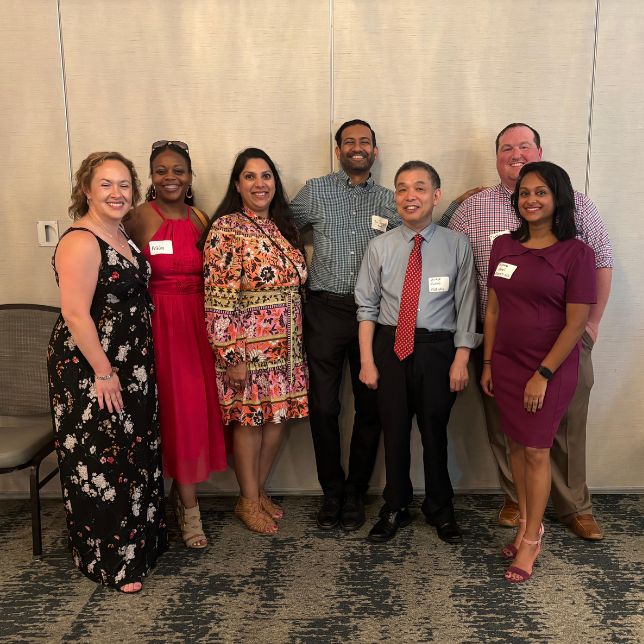 Seven alumni wearing name tags stand together smiling at a PCOM reunion gathering