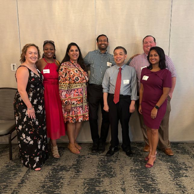 Seven alumni wearing name tags smile together at a PCOM reunion gathering