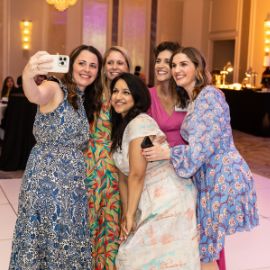 Five women in colorful dresses pose for a group selfie at a PCOM alumni ballroom event