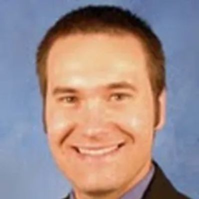 Curtis Grenoble smiling in a professional headshot wearing a dark suit against a blue background