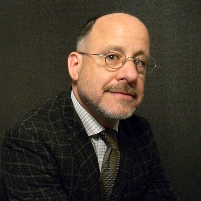David Lipten smiling in a professional headshot wearing a plaid blazer, tie, and wire-rimmed glasses
