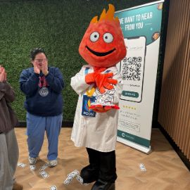 PCOM flame mascot wearing a white coat poses next to a student at a campus engagement event
