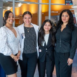 Four women pose together smiling in a modern campus lobby at a PCOM Georgia event