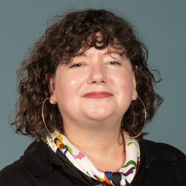 Woman with curly hair and hoop earrings smiling in a professional headshot against a blue-gray background