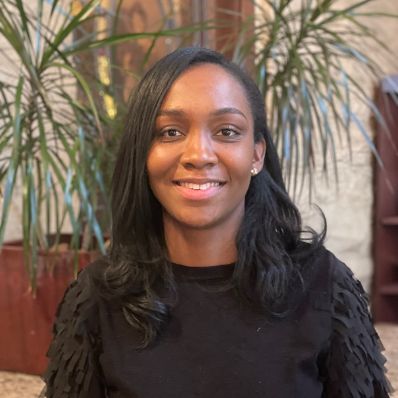 Krystal Carter smiling in a headshot wearing a black top with greenery in the background