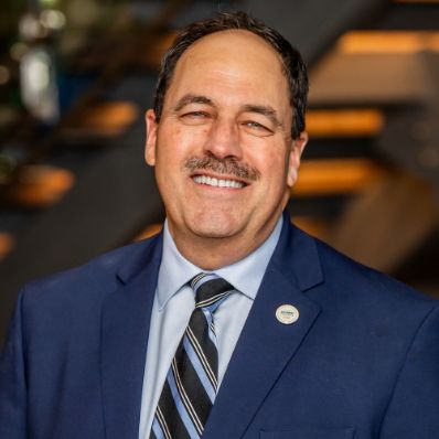 Paul LaPoint smiling in a professional headshot wearing a navy blazer and striped tie in a modern building lobby