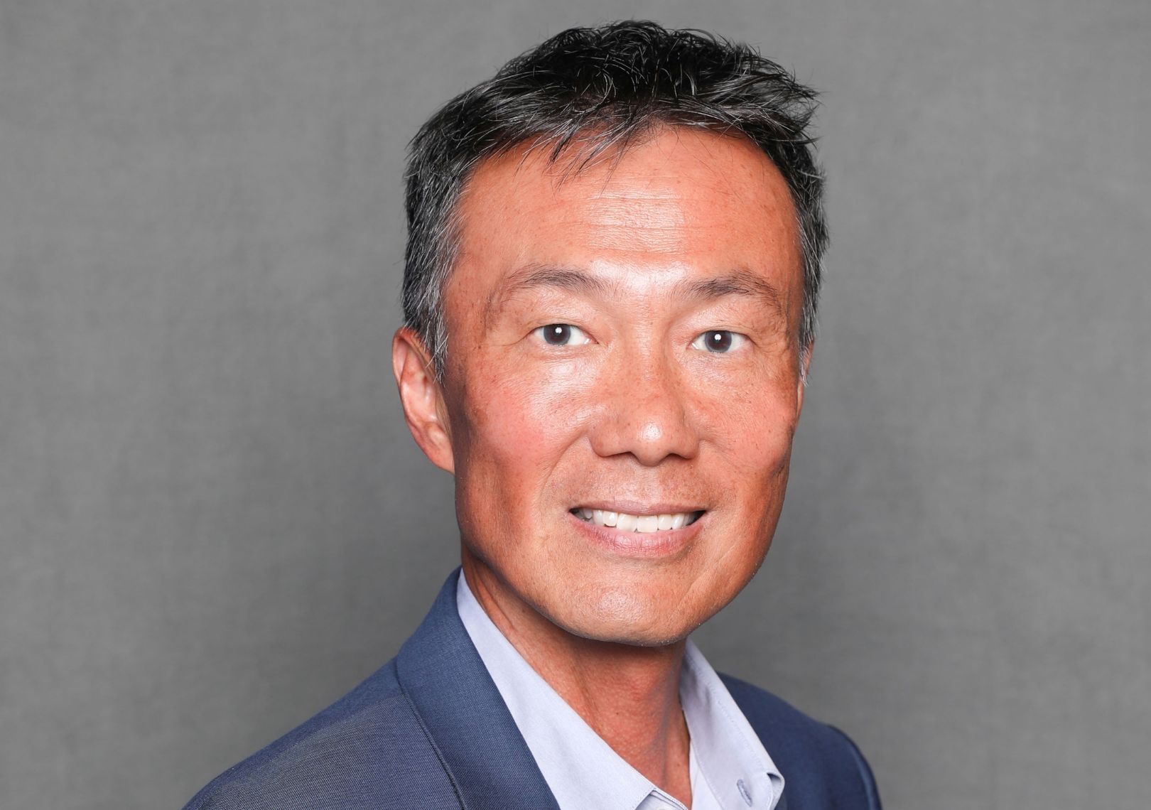 Man in a blue blazer smiling in a professional headshot against a gray background