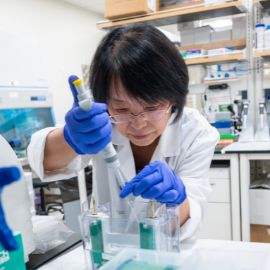 Researcher in a white coat and blue gloves uses a pipette in a laboratory setting