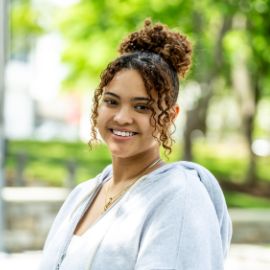 Young woman with curly hair smiling outdoors on a green tree-lined campus