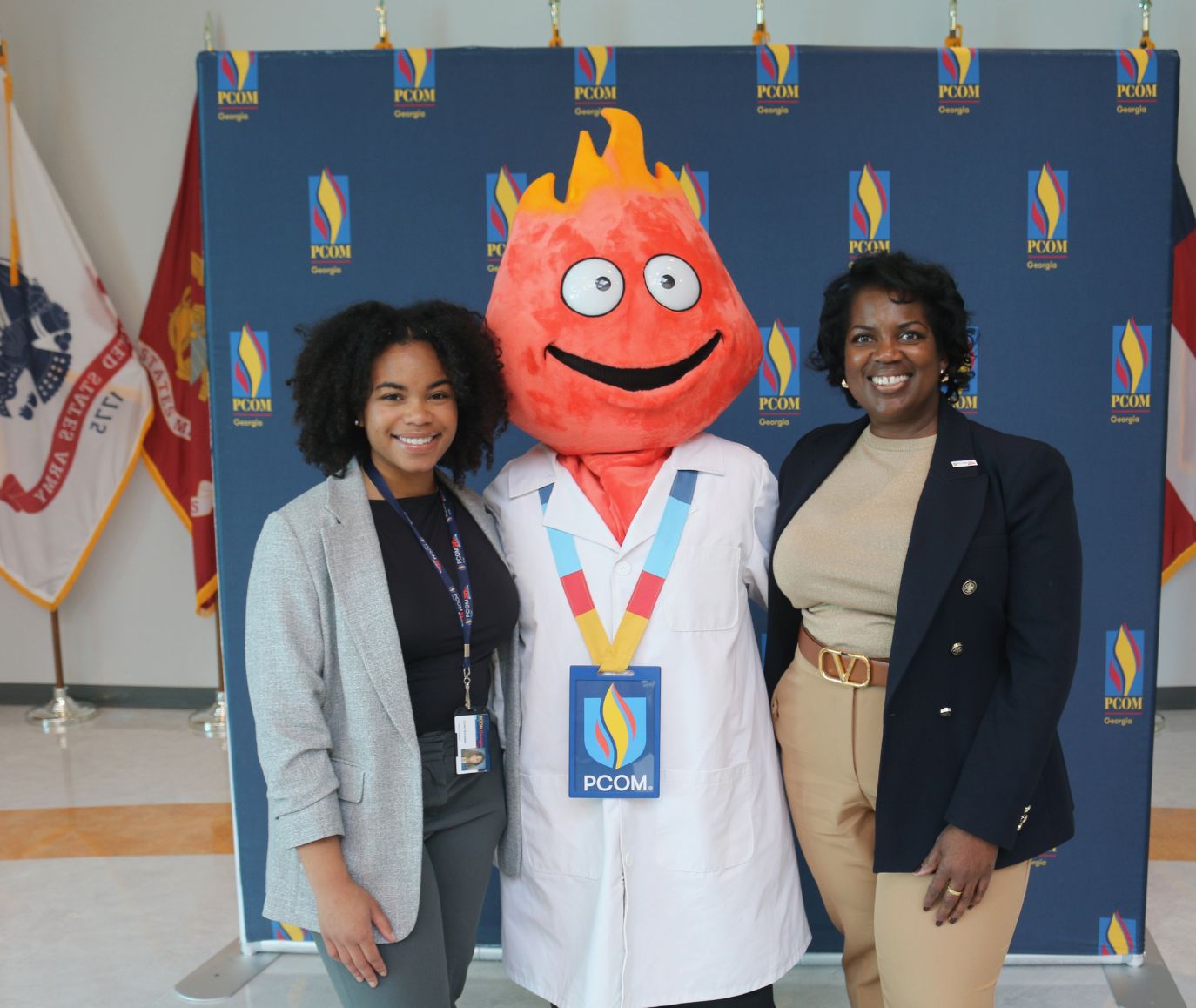 Two staff members pose with the PCOM Finny Flame mascot in front of a PCOM Georgia branded backdrop
