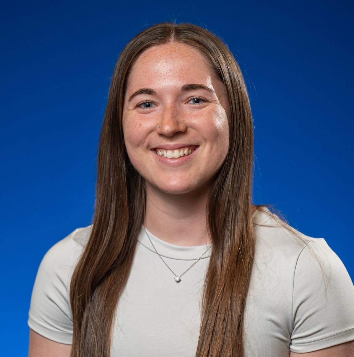 Young woman with long brown hair smiling in a headshot against a blue background