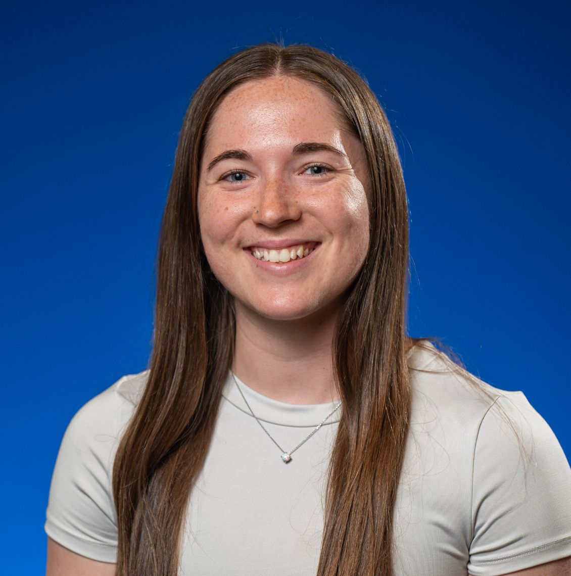 Young woman with long brown hair smiling in a headshot against a blue background
