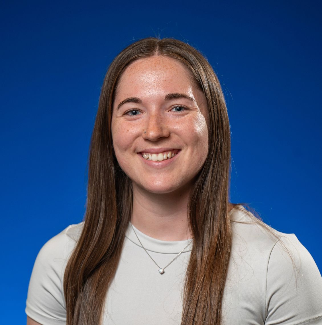 Young woman with long brown hair smiling in a headshot against a blue background