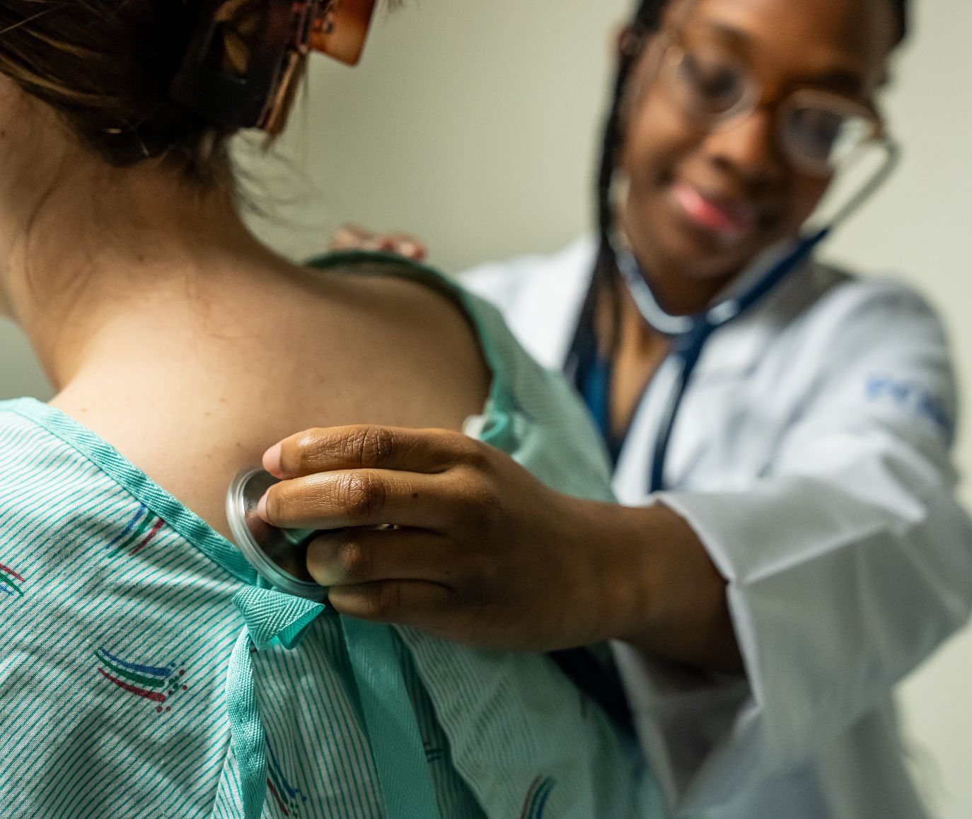 Medical student in a white coat places a stethoscope on a patient's back during a clinical exam