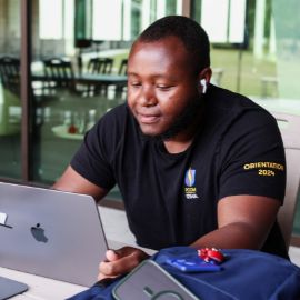 Student in a PCOM orientation t-shirt works on a laptop at a campus study area