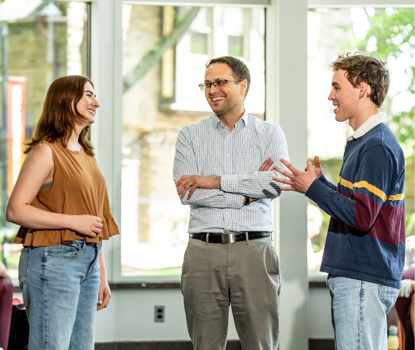 Two students and a faculty member laugh together during a conversation in a bright campus atrium