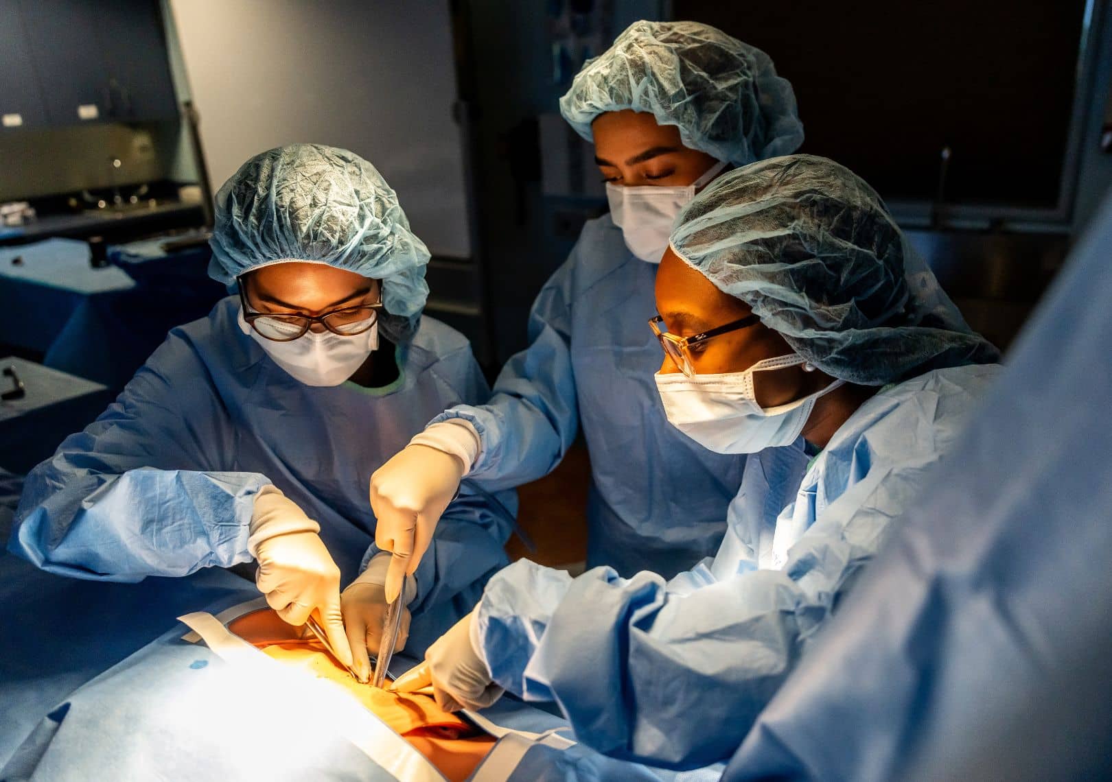 Three medical students in scrubs, masks, and surgical caps practice a procedure in a simulation lab