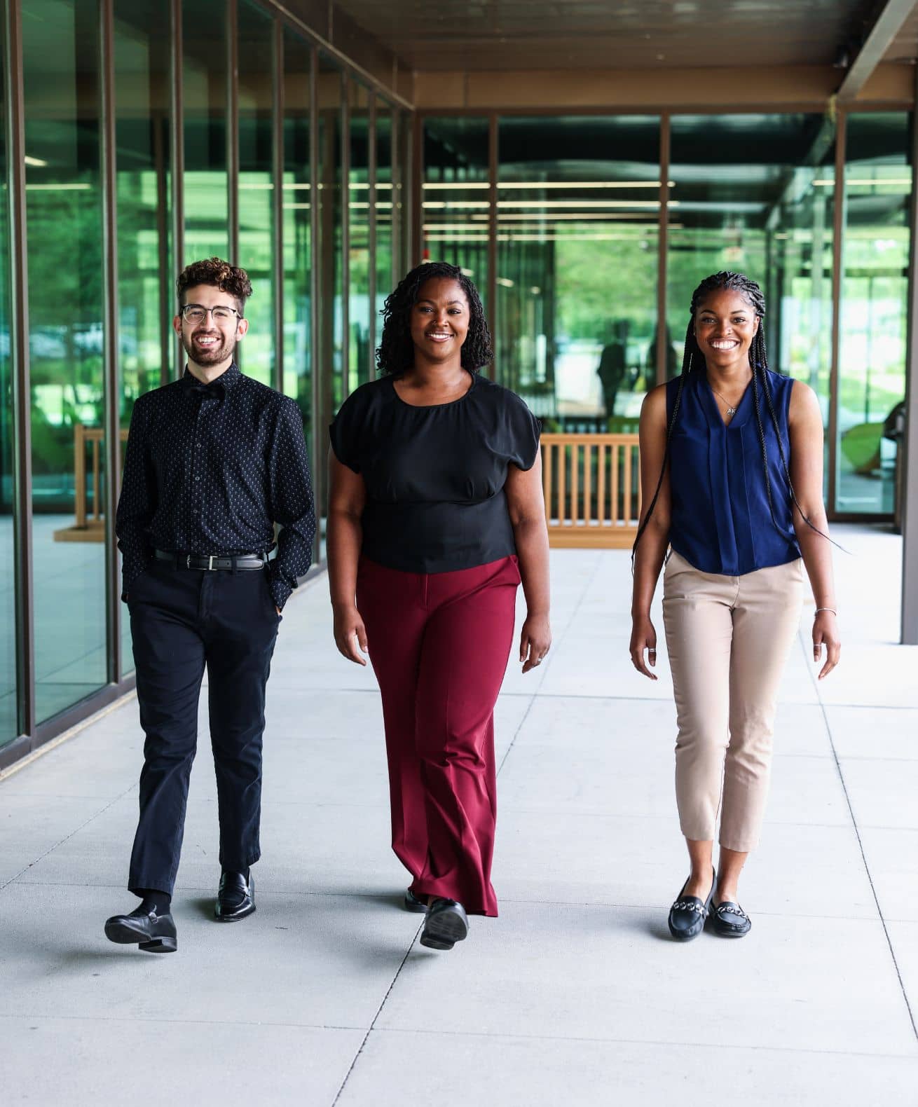 Three students walk side by side smiling through a glass-walled campus walkway