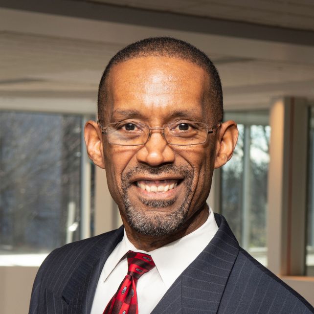 Tony Smith smiling in a professional headshot wearing a pinstripe suit and red tie in an office setting