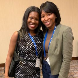 Two women wearing conference lanyards smile together at a PCOM event