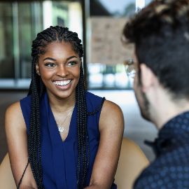 Woman with braids in a navy blouse smiling during a one-on-one conversation in a modern office setting
