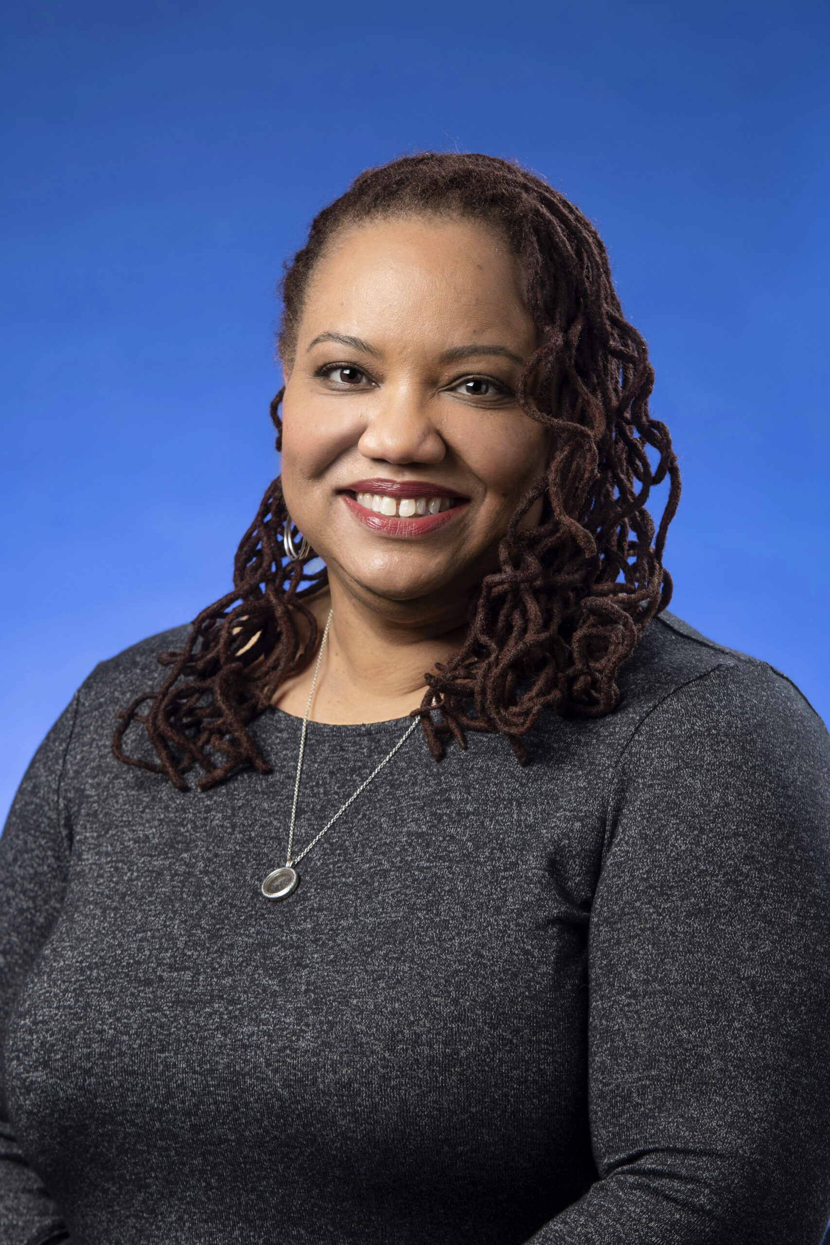Woman smiling in a a gray sweater against a blue background